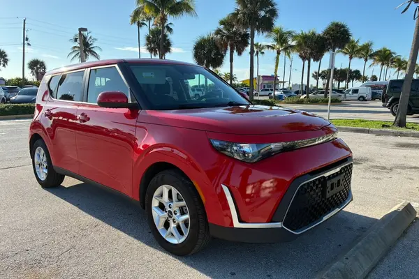 Red 2024 Kia Soul, front three-quarter view from the passenger side, parked in a palm-lined lot