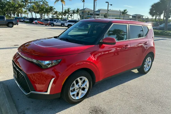 Red 2024 Kia Soul, front three-quarter view from the driver's side in a sunny parking lot with palm trees