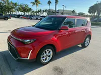 Red 2024 Kia Soul, front three-quarter view from the driver's side in a sunny parking lot with palm trees
