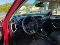 2024 Kia Soul interior seen through the open driver's door, with steering wheel, touchscreen and dark cloth seats