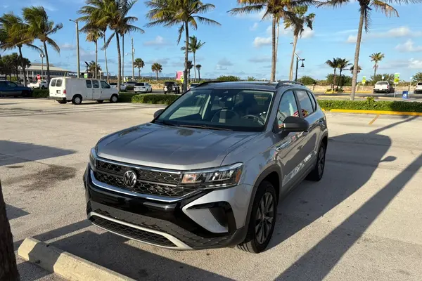 Silver 2023 Volkswagen Taos SUV, front driver-side three-quarter view, parked in a palm-lined beachside lot