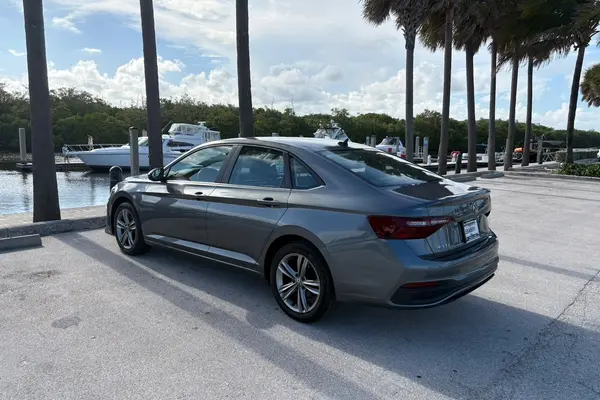 Gray 2024 Volkswagen Jetta sedan, rear driver-side three-quarter view, parked at a palm-lined marina with boats docked behind it