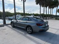 Gray 2024 Volkswagen Jetta sedan, rear driver-side three-quarter view, parked at a palm-lined marina with boats docked behind it