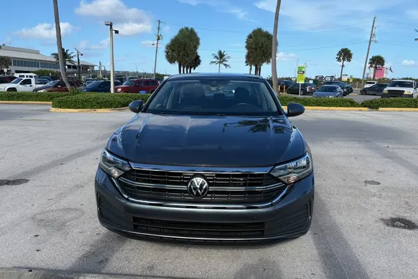 Gray 2024 Volkswagen Jetta sedan seen head-on, showing the Volkswagen badge, chrome-trimmed grille, and LED headlights
