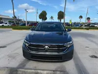 Gray 2024 Volkswagen Jetta sedan seen head-on, showing the Volkswagen badge, chrome-trimmed grille, and LED headlights