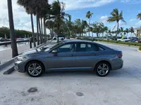Gray 2024 Volkswagen Jetta sedan in driver-side profile, showing its alloy wheels, parked at a palm-lined marina